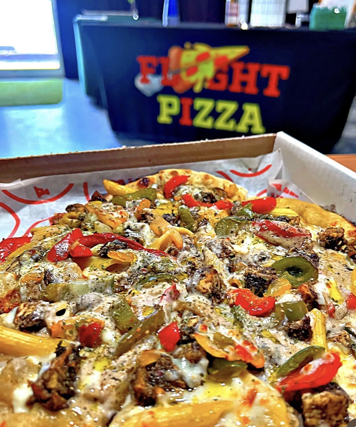 A loaded Flyght Pizza pie in a box, topped with peppers and herbs